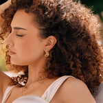 Boucles d'oreilles dorées en acier inoxydable, motif hippocampe et étoile de mer, portées par une femme.