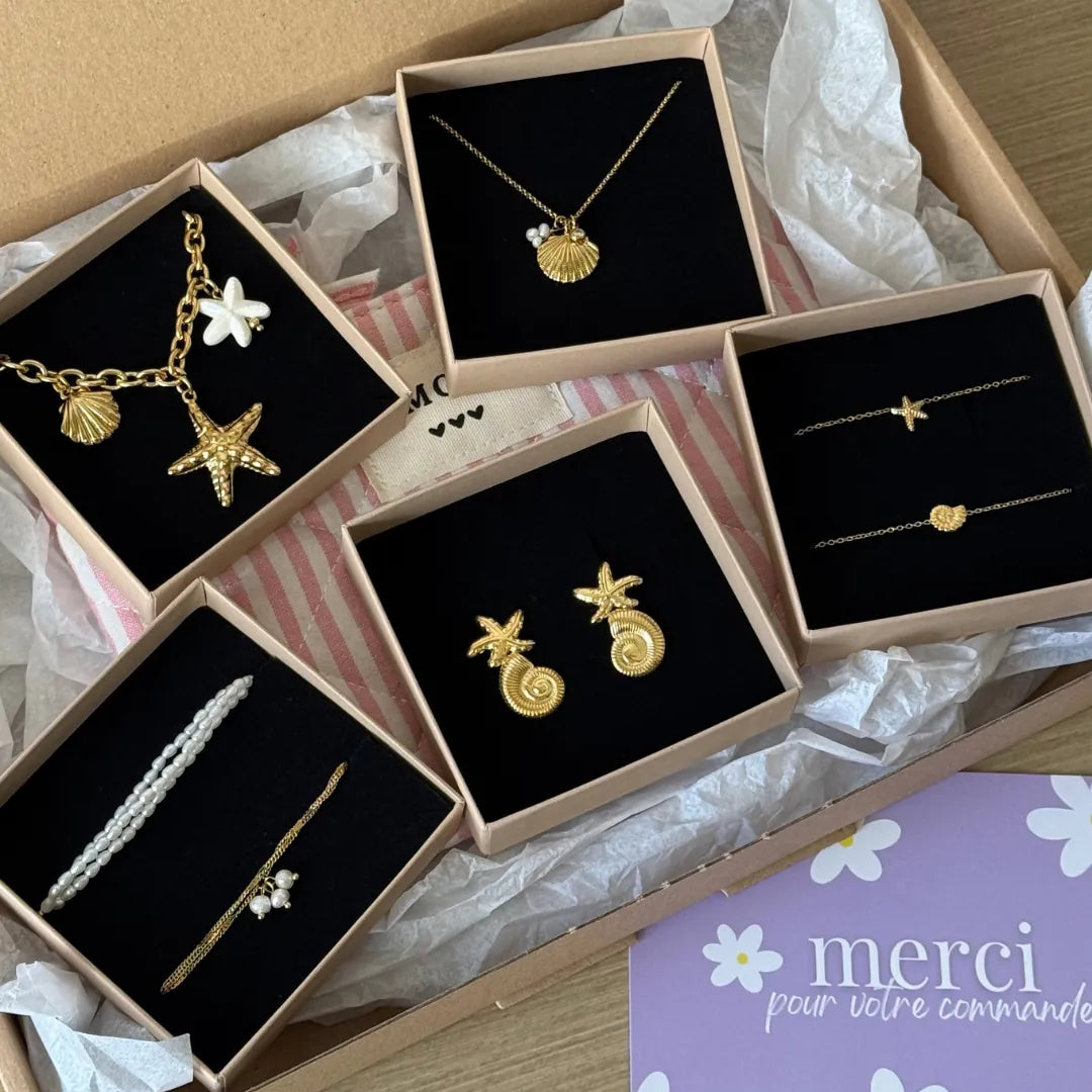 Boucles d'oreilles en acier inoxydable doré, design étoile de mer et coquillage, présentées sur fond noir.