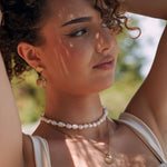 Boucles d'oreilles pendantes double coquillage doré en acier inoxydable, portées par une femme.