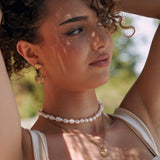 Boucles d'oreilles pendantes double coquillage doré en acier inoxydable, portées par une femme.