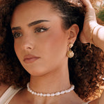 Boucles d'oreilles pendantes en acier inoxydable couleur or, design double coquillage texturé, portées sur oreille femme.