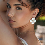 Boucles d'oreilles acier inoxydable, motif fleur blanche nacrée 4 pétales avec cœur doré, sur l'oreille d'une femme.