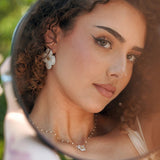 Boucles d'oreilles fleur blanche en acier inoxydable, centre doré, portées par une femme.