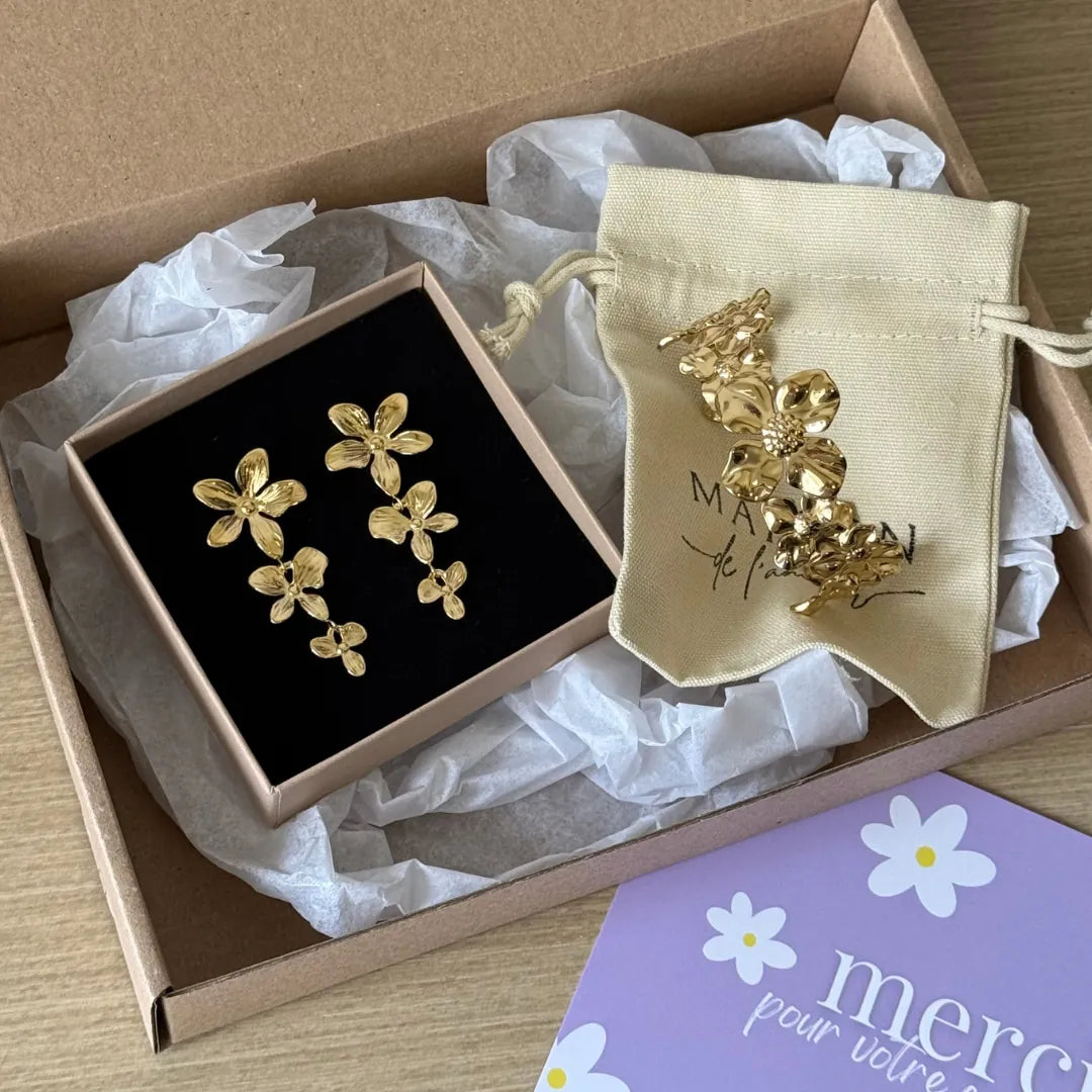 Boucles d'oreilles pendantes en acier inoxydable doré, formées de trois fleurs. Présentées dans une boîte avec un pochon et