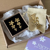 Boucles d'oreilles pendantes en acier inoxydable doré, formées de trois fleurs. Présentées dans une boîte avec un pochon et
