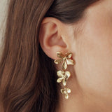 Boucles d'oreilles pendantes 3 fleurs en acier inoxydable doré sur l'oreille d'une femme.