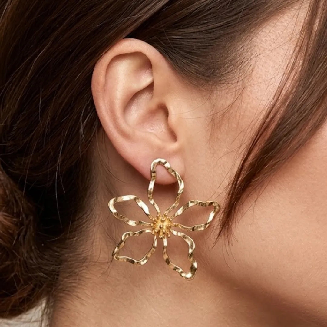 Boucles d'oreilles fleurs martelées en acier inoxydable doré, portées par une femme.