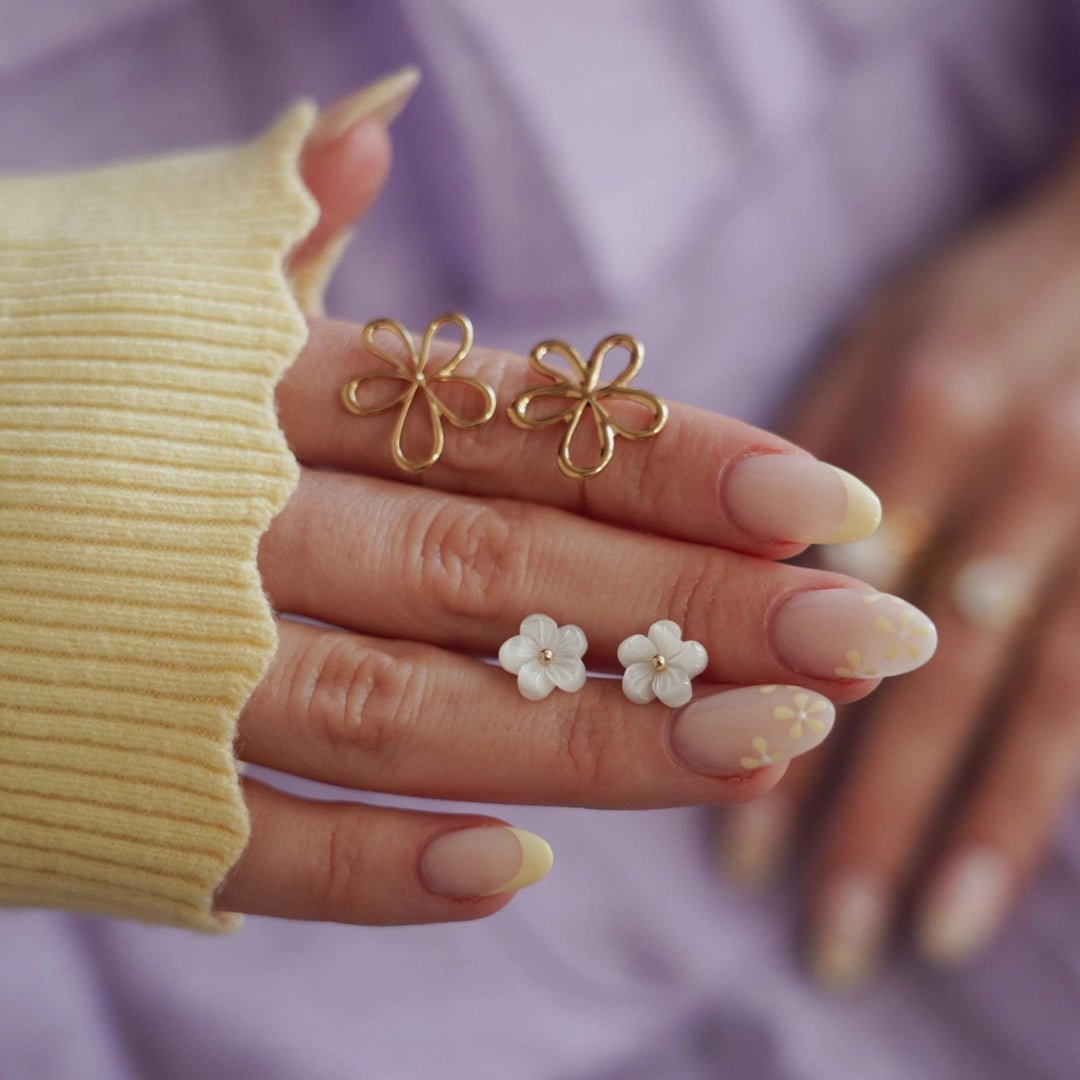 Boucles d'oreilles acier inoxydable: 2 paires, fleurs dorées ajourées et fleurs blanches nacrées, sur main.