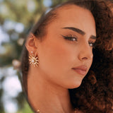 Boucles d'oreilles soleil en acier inoxydable doré avec perle centrale, sur l'oreille d'une femme.