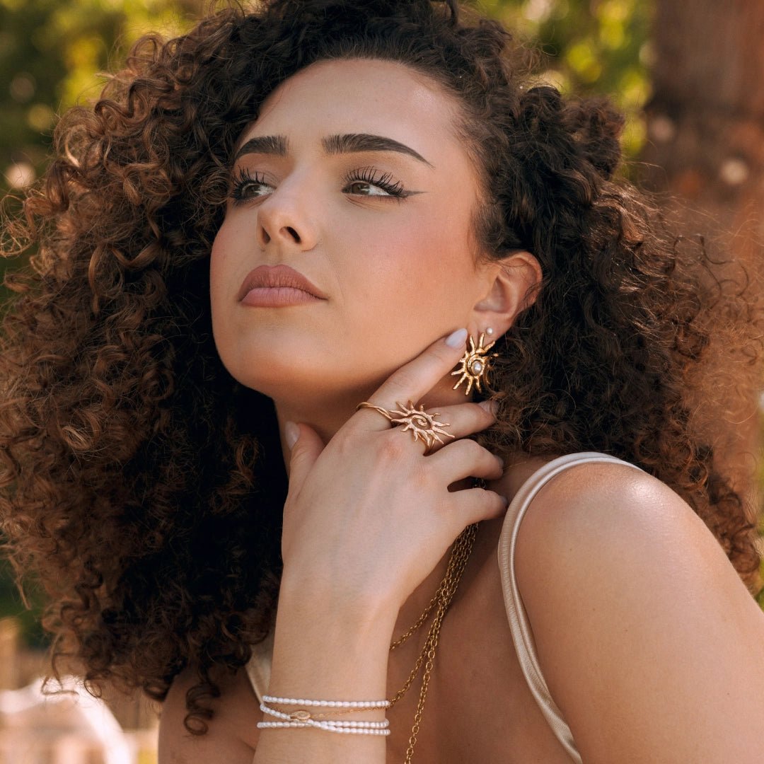 Boucles d'oreilles soleil œil maléfique en acier inoxydable doré, portées par femme aux boucles.