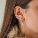 Gros plan sur une oreille avec trois boucles d'oreilles en acier inoxydable doré : une créole avec zirconium poire, une puce
