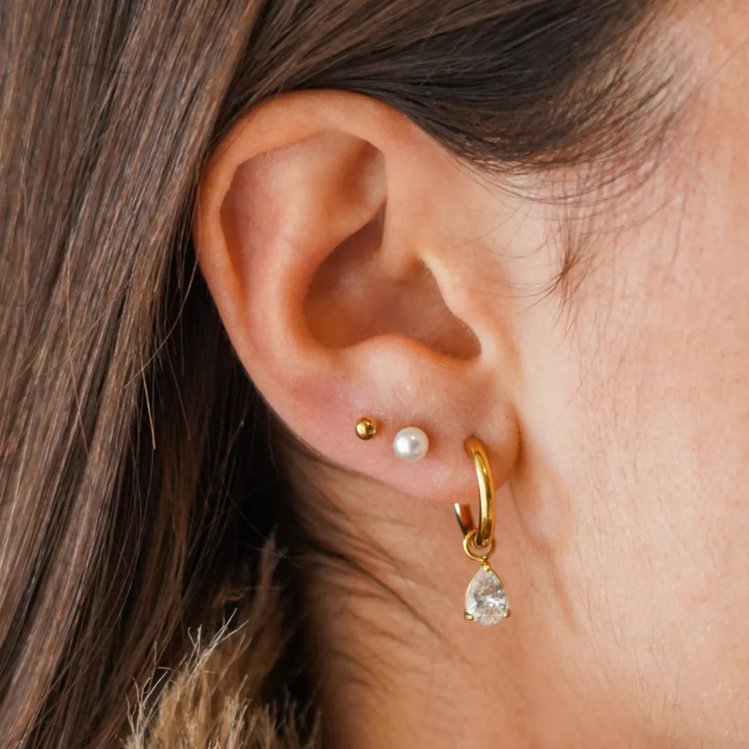 Femme portant trois boucles d'oreilles: une puce acier inoxydable doré, une perle et une créole zirconium poire.