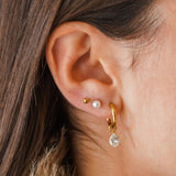Femme portant trois boucles d'oreilles: une puce acier inoxydable doré, une perle et une créole zirconium poire.