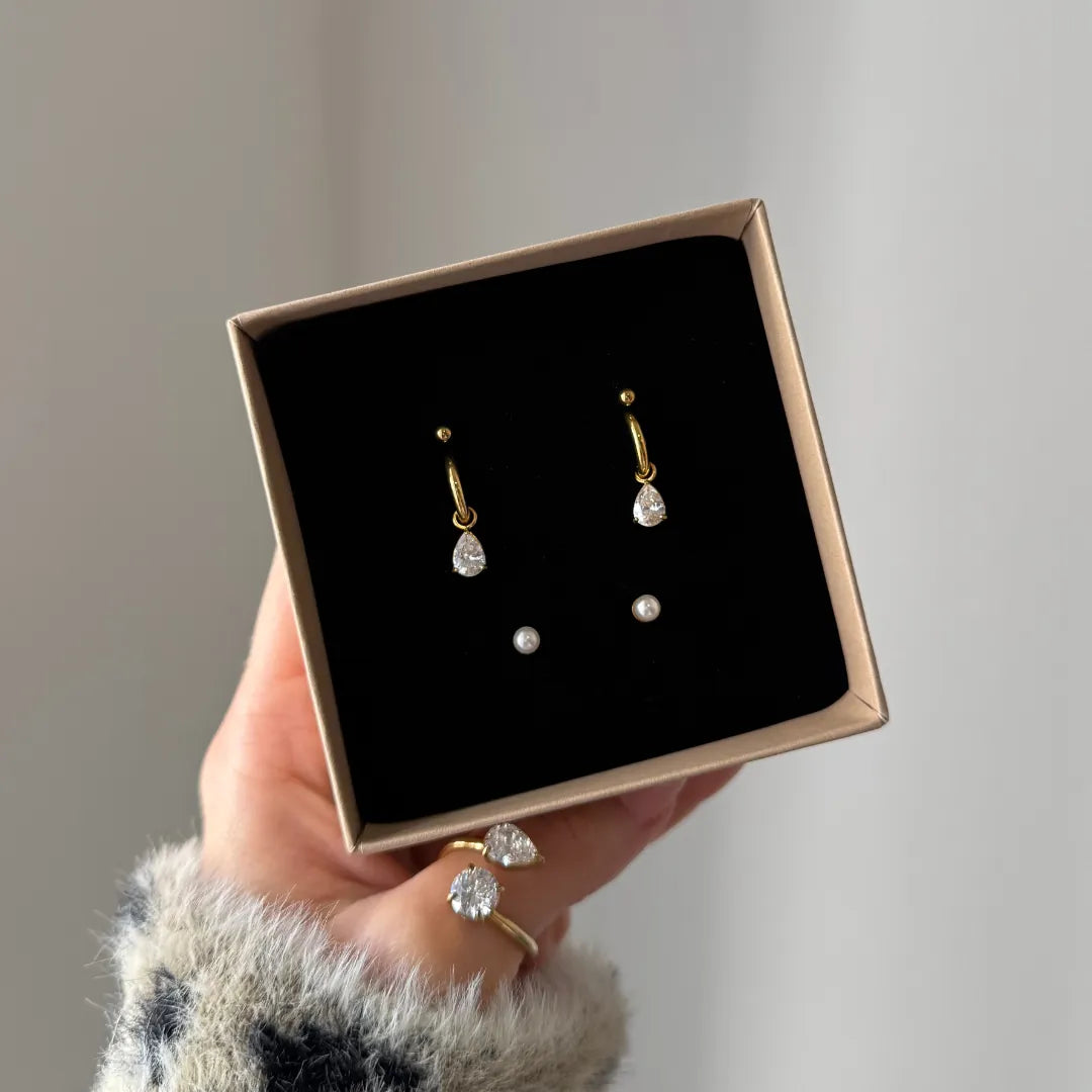 Trois paires de boucles d'oreilles en acier inoxydable doré dans un écrin : créoles zirconium poire, perles rondes et puces