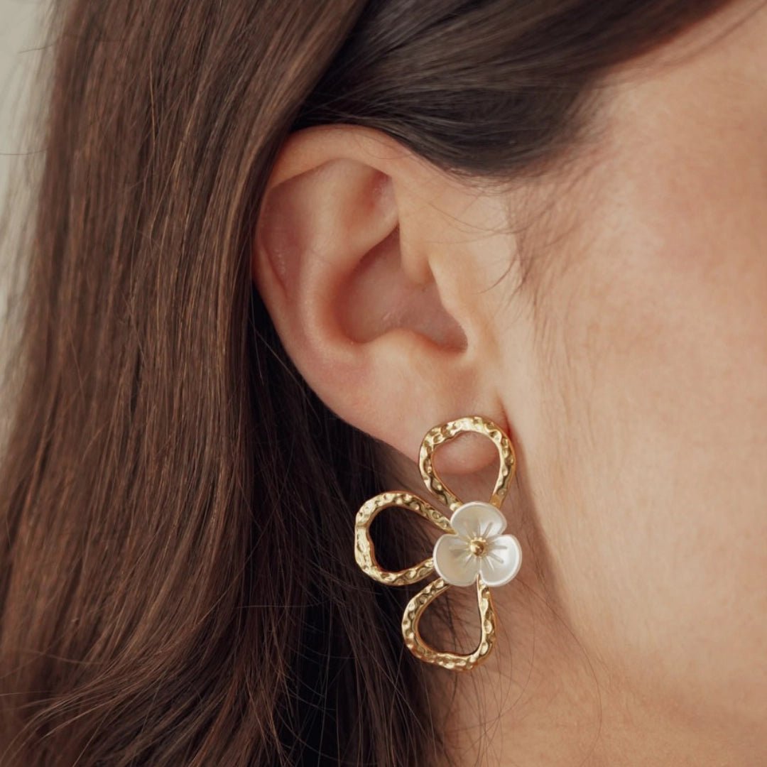 Boucles d'oreilles fleur en acier inoxydable doré martelé, centre nacré, portées sur l'oreille d'une femme.