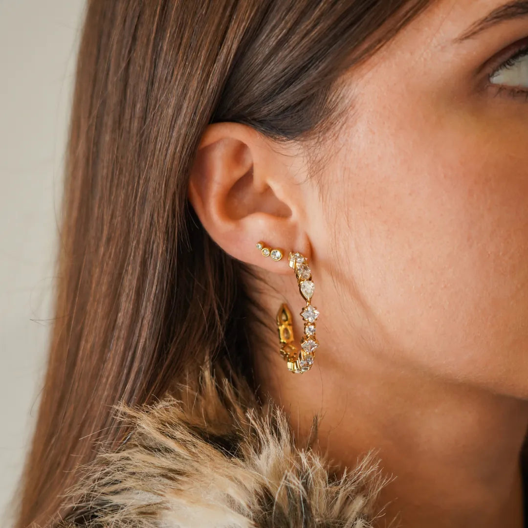 Oreille de femme. Piercing en acier inoxydable doré à trois zircons et créole dorée sertie de zircons variés.