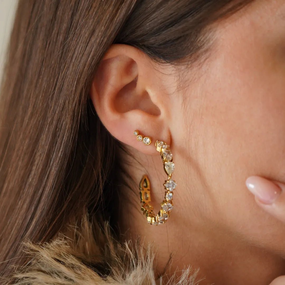 Piercing d'oreille en acier inoxydable doré avec trois zircons gradués, et créole dorée avec zircons sur une oreille.
