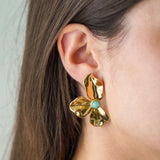 Boucle d'oreille fleurie en acier inoxydable doré texturé, centrée d'une pierre naturelle turquoise.