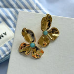 Deux boucles d'oreilles en acier inoxydable doré texturé, forme fleur avec une pierre naturelle turquoise au centre.