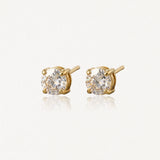 Paire de clous d'oreilles en or jaune avec pierres rondes incolores à facettes, sur fond clair et réfléchissant.