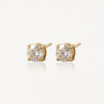 Paire de clous d'oreilles en or jaune avec pierres rondes incolores à facettes, sur fond clair et réfléchissant.