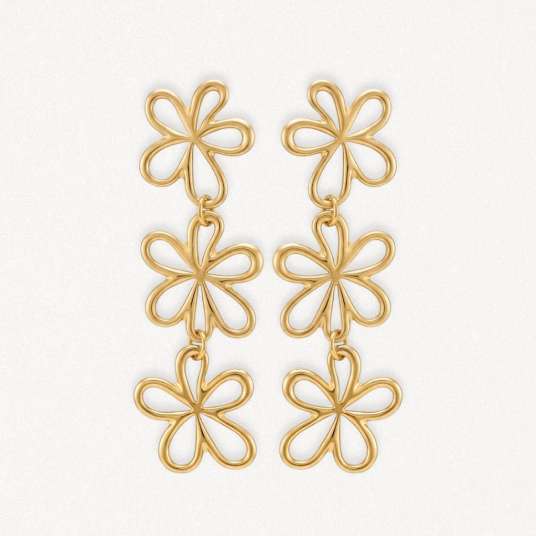 Boucles d'oreilles pendantes en acier inoxydable doré, motif 3 fleurs stylisées reliées, fond blanc.