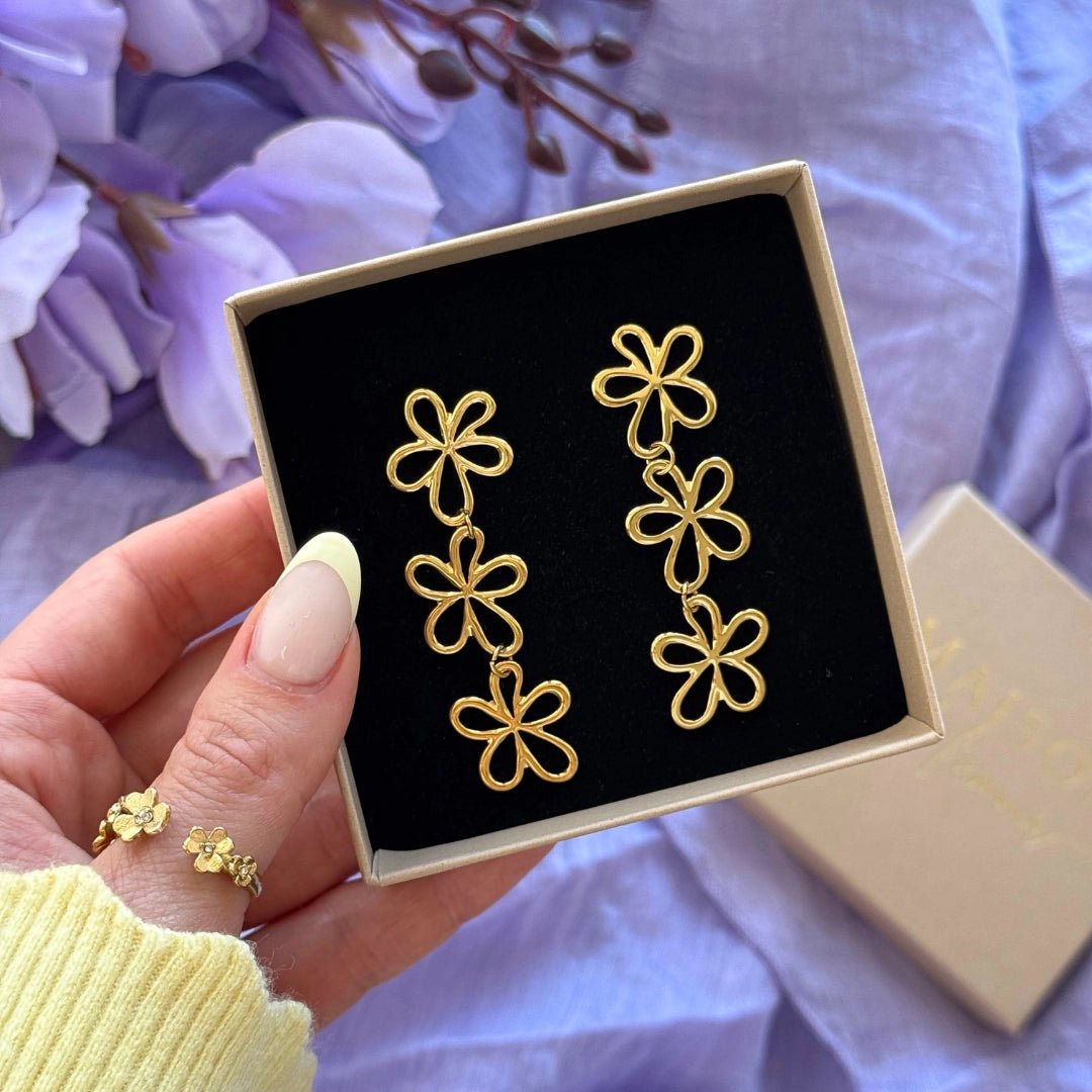 Boucles d'oreilles pendantes en acier inoxydable couleur or, motif 3 fleurs ajourées, présentées dans leur boîte.