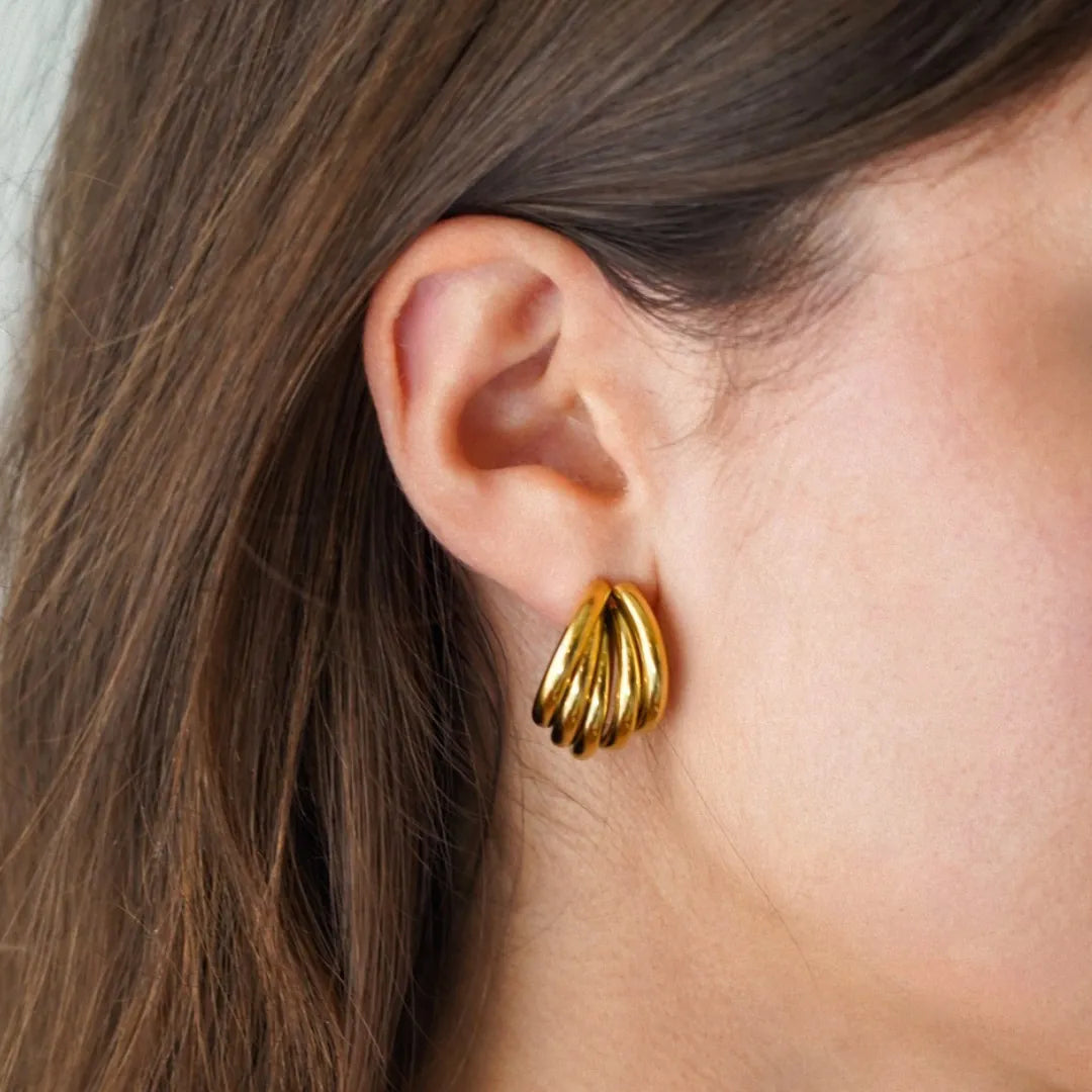 Boucle d'oreille en acier inoxydable doré, design à bandes arrondies, portée sur une oreille.