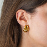 Boucle d'oreille en acier inoxydable doré, design à bandes arrondies, portée sur une oreille.