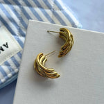 Paire de boucles d'oreilles en acier inoxydable doré de 2,5 cm, design C formé de bandes ondulées, posées sur fond blanc.