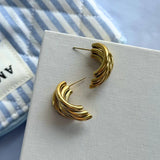 Paire de boucles d'oreilles en acier inoxydable doré de 2,5 cm, design C formé de bandes ondulées, posées sur fond blanc.