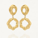 Une paire de boucles d'oreilles dorées Arlette en acier inoxydable. Chaque boucle est formée de deux éléments asymétriques et texturés, reliés par un petit anneau, sur un fond blanc avec une légère réflexion.