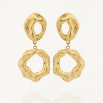 Une paire de boucles d'oreilles dorées Arlette en acier inoxydable. Chaque boucle est formée de deux éléments asymétriques et texturés, reliés par un petit anneau, sur un fond blanc avec une légère réflexion.