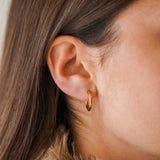Mini créole ronde en acier inoxydable doré portée à l'oreille d'une femme aux cheveux bruns.