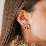 Trois boucles d'oreilles sur une oreille: une puce brillante, une mini créole en acier inoxydable doré et une créole avec