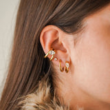 Oreille de femme portant un ear cuff, une puce et deux mini créoles en acier inoxydable doré. Certains ont des éléments
