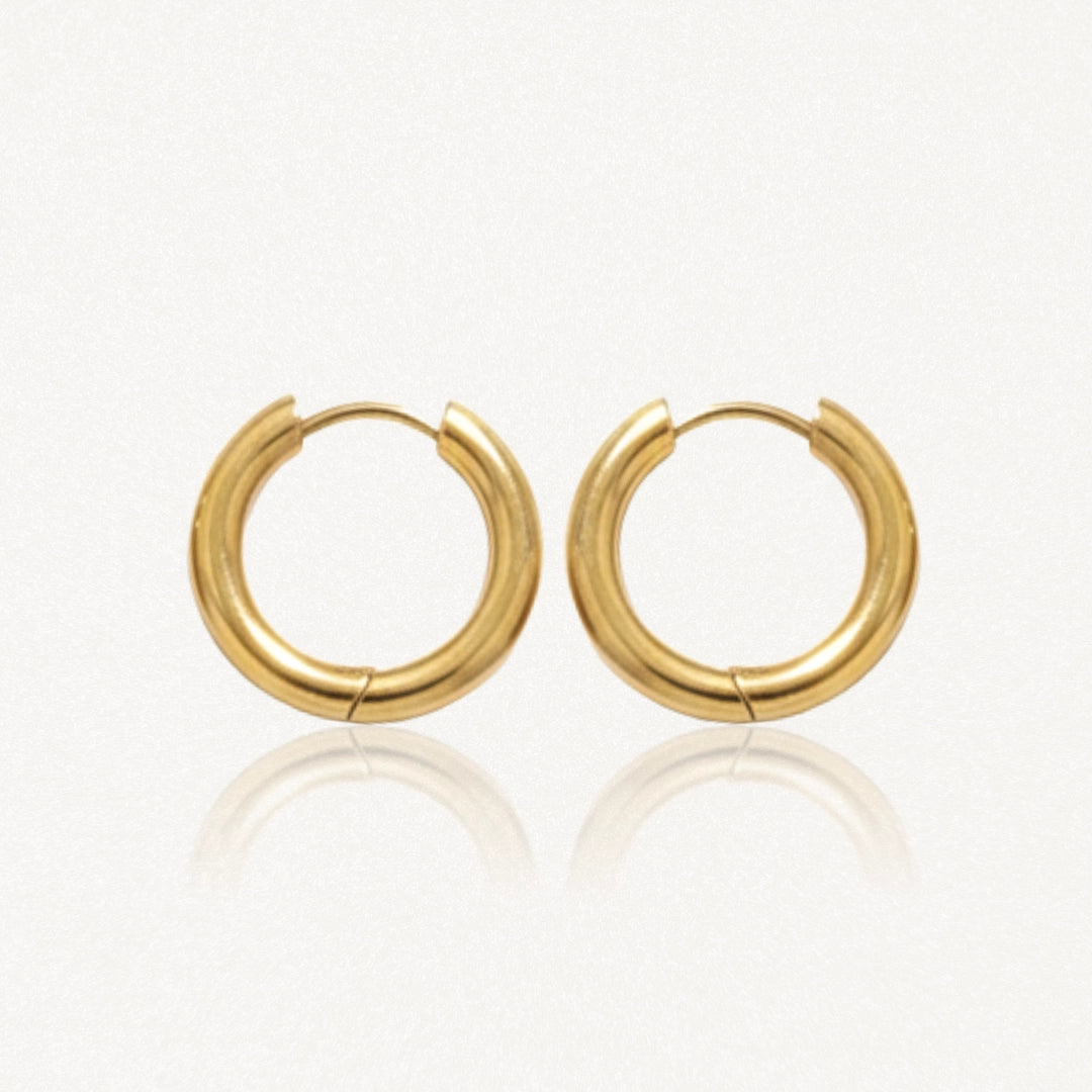 Paire de boucles d'oreilles créoles épaisses et dorées, brillantes, posées sur un fond clair avec reflets.
