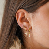 Trois boucles d'oreilles en acier inoxydable doré portées : une puce, une croix et une barrette serties de zirconium.