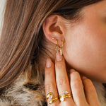 Trois boucles d'oreilles acier inoxydable doré sur une oreille : une puce boule, une créole avec croix zirconium, une créole
