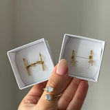 Main tenant deux boîtes blanches. Boucles d'oreilles en acier inoxydable doré et zirconium : une paire barrette, une paire