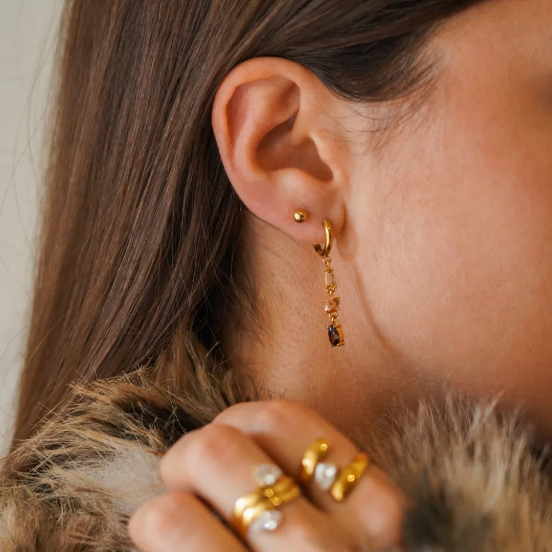 Créole pendante en acier inoxydable doré, avec une cascade de zircons champagne et marron, portée à l'oreille d'une femme.