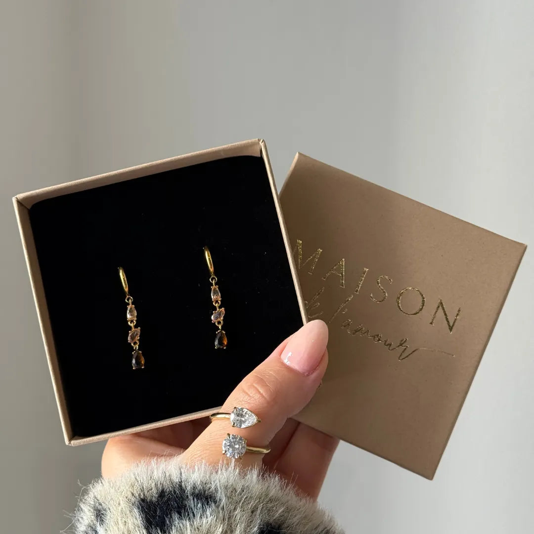 Deux boucles d'oreilles créoles pendantes en acier inoxydable doré avec une cascade de zircons champagne et marron, dans une