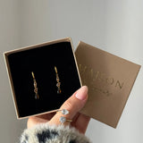 Deux boucles d'oreilles créoles pendantes en acier inoxydable doré avec une cascade de zircons champagne et marron, dans une