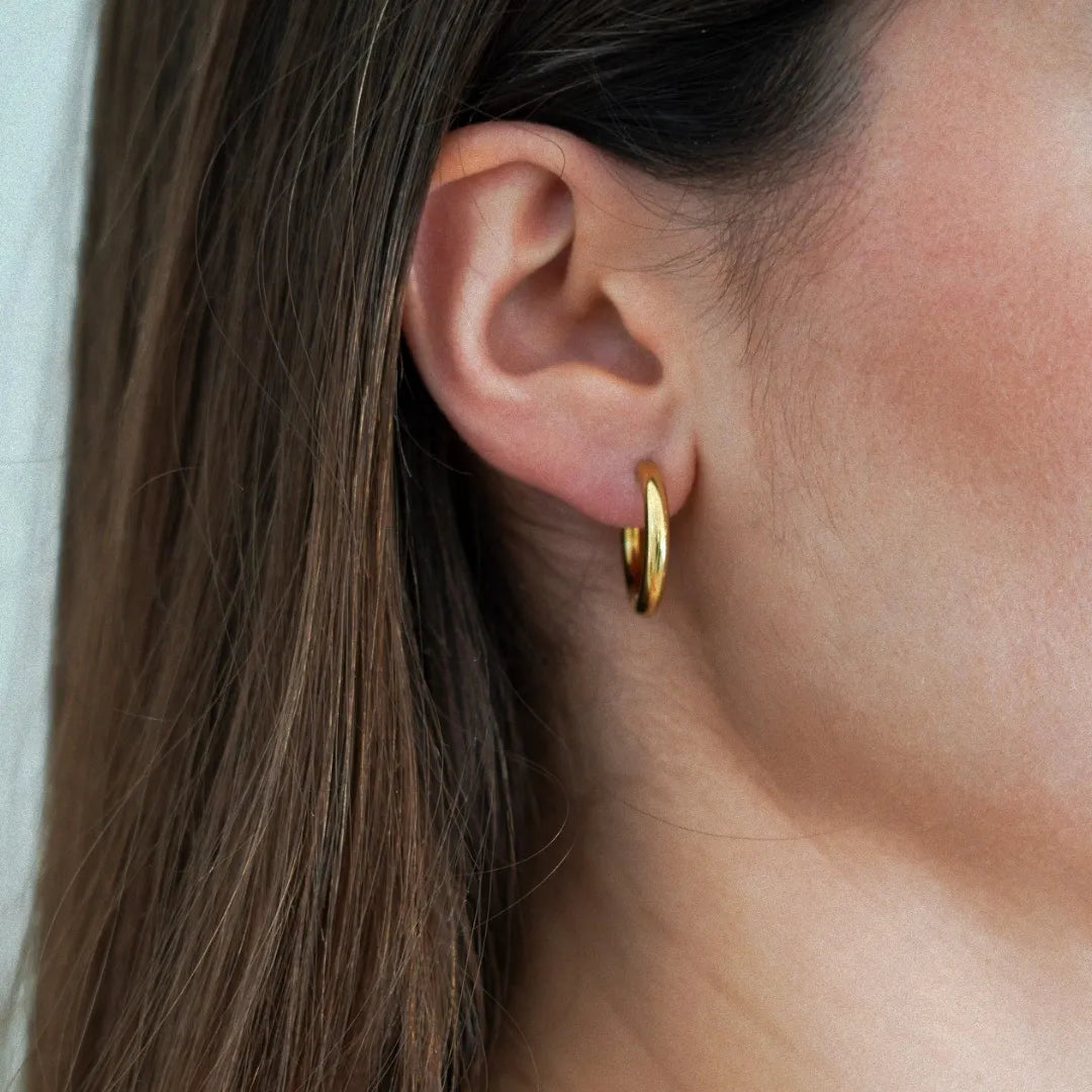 Gros plan sur l'oreille d'une femme portant une créole dorée lisse et brillante. Cheveux châtains sur le côté.