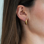 Gros plan sur l'oreille d'une femme portant une créole dorée lisse et brillante. Cheveux châtains sur le côté.