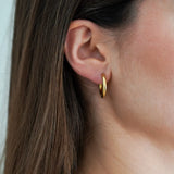 Gros plan sur l'oreille d'une femme portant une créole dorée lisse et brillante. Cheveux châtains sur le côté.