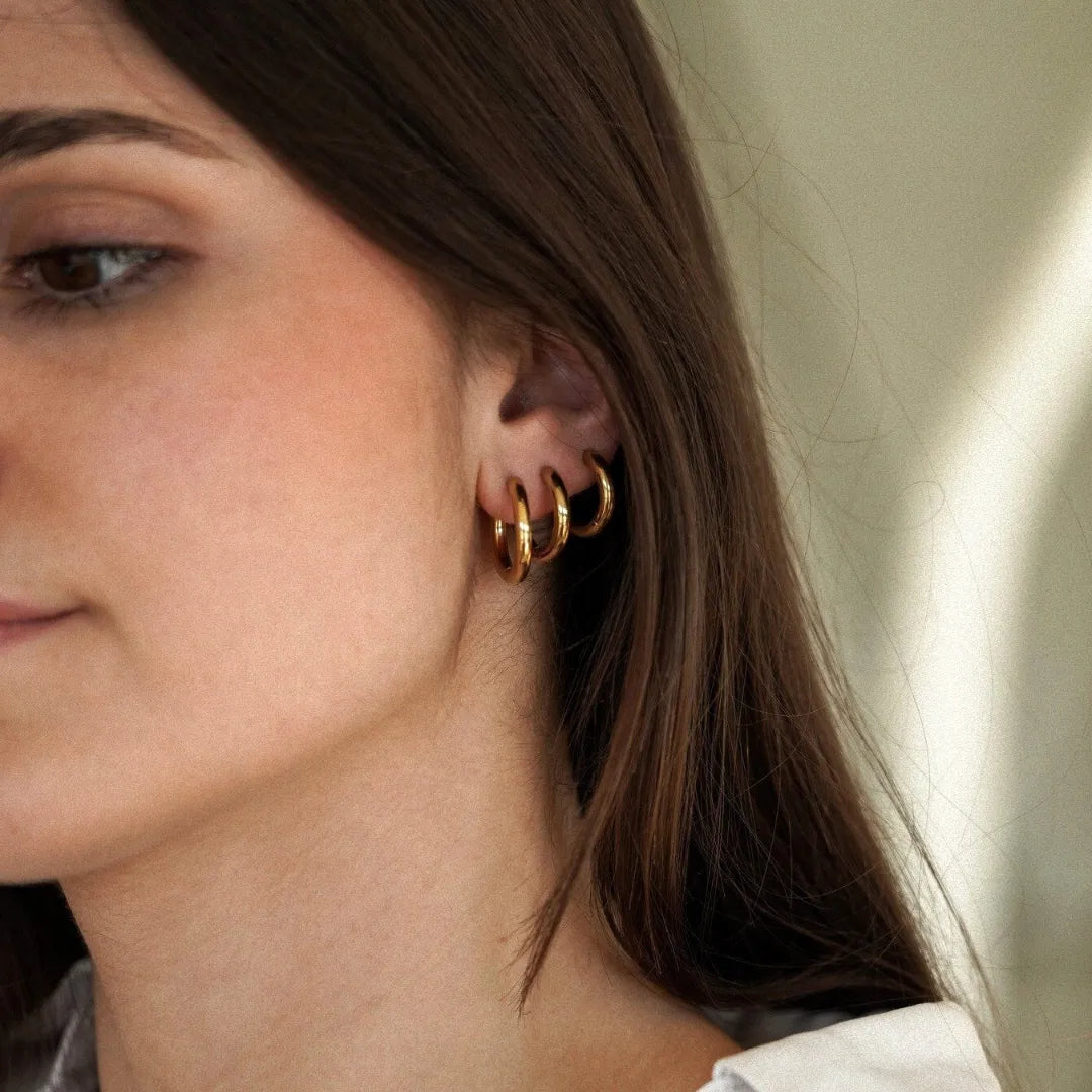 Gros plan sur l'oreille droite d'une femme, ornée de trois boucles d'oreilles anneaux dorés lisses et brillants.