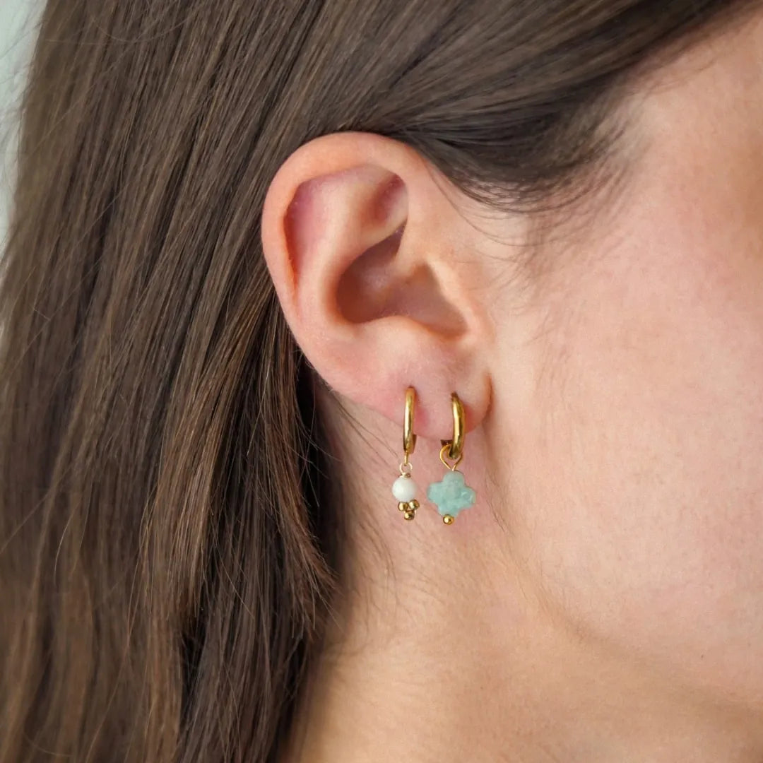 L'oreille d'une femme porte deux créoles en acier inoxydable doré, l'une ornée d'une perle, l'autre d'une pierre naturelle
