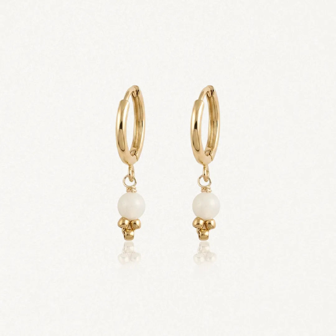 Deux boucles d'oreilles créoles en acier inoxydable doré, avec une bille ronde blanche et trois petites billes dorées en