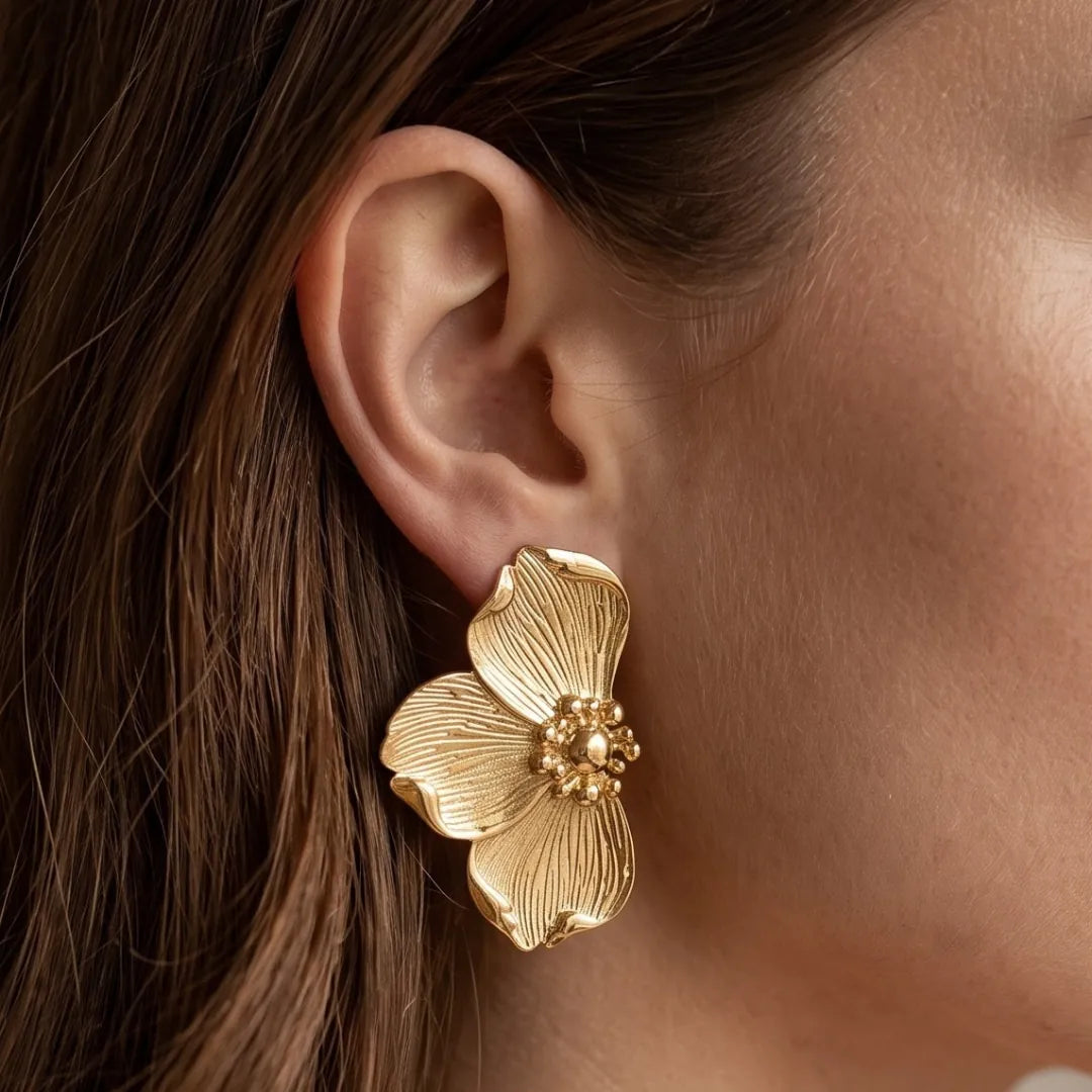 Boucle d'oreille en acier inoxydable doré, en forme de fleur avec des pétales texturés et un centre granuleux, portée sur une